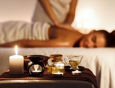 Aromatherapy oils and candles with lady receiving massage in background